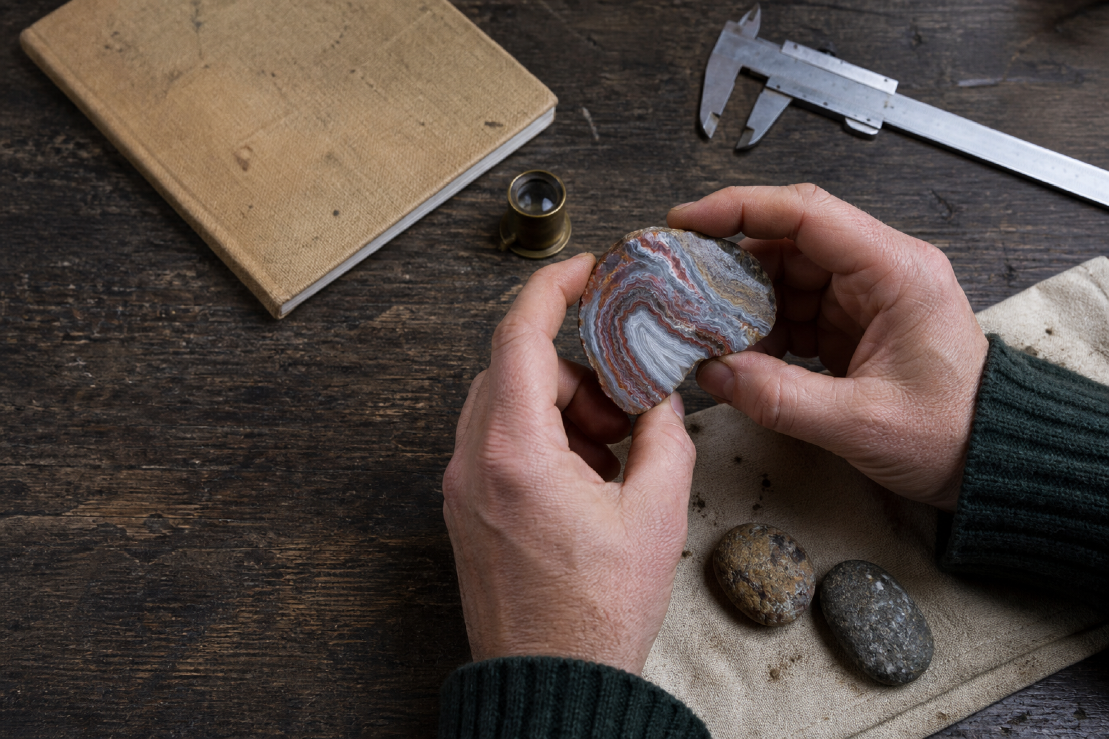 Hands inspecting a banded agate at a geologist's workbench